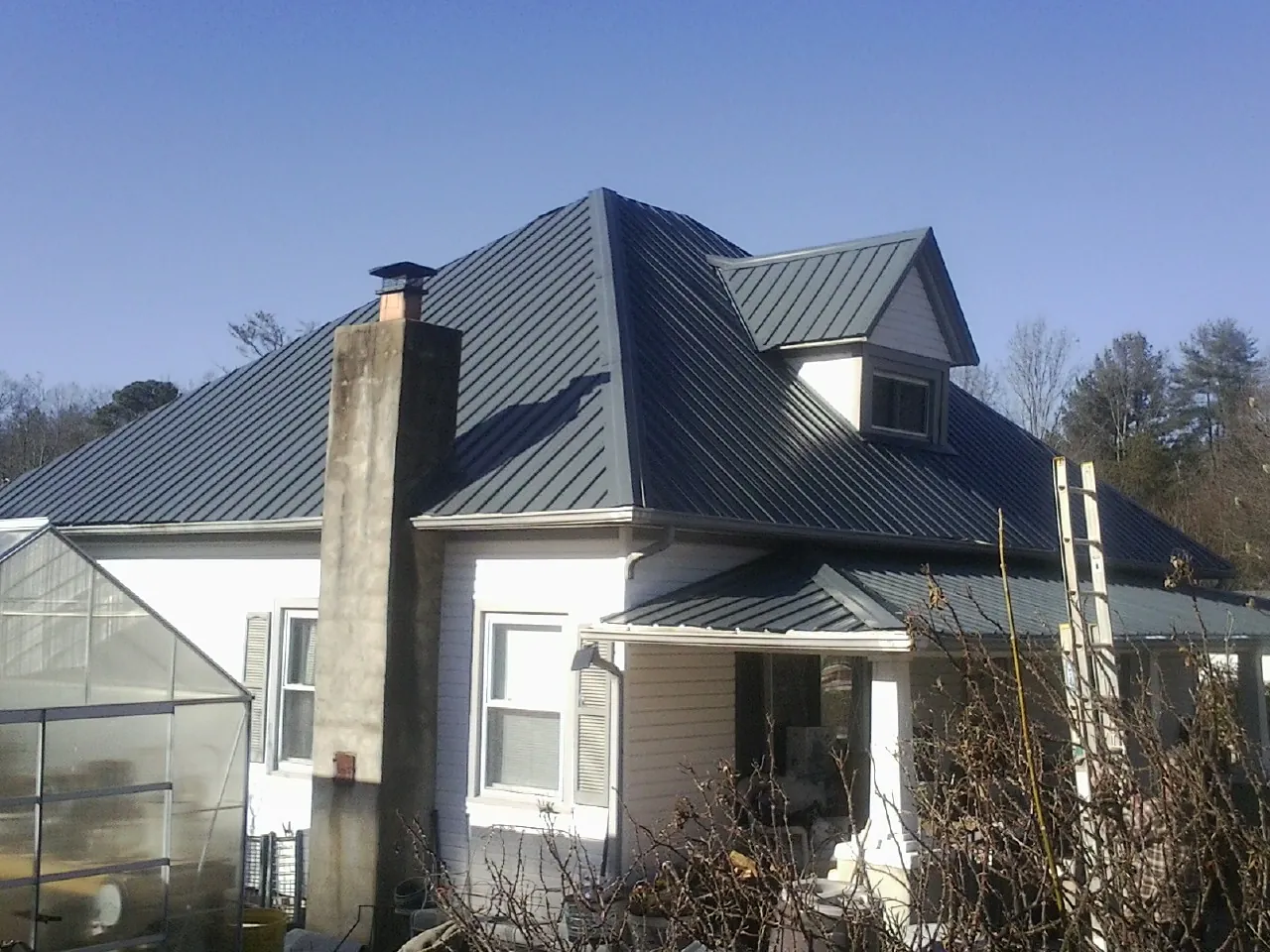 Dark blue standing seam metal roof on a white farmhouse with dormer — Slate & Tile Roof Repair by Roofing Brothers in Douglasville