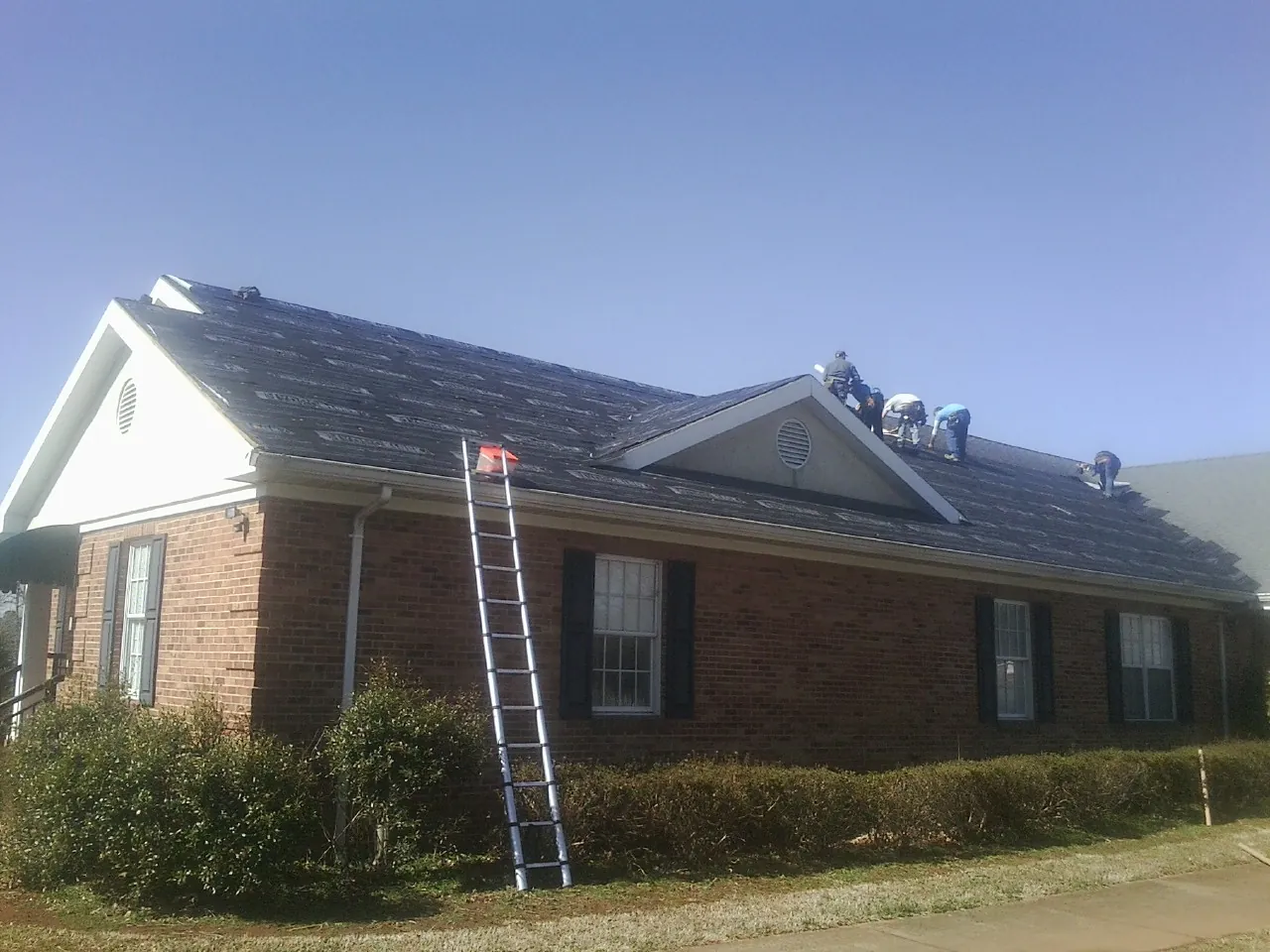 Crew tearing shingles off a brick ranch roof with a ladder set — Metal Roof Repair work by our crew in Douglasville