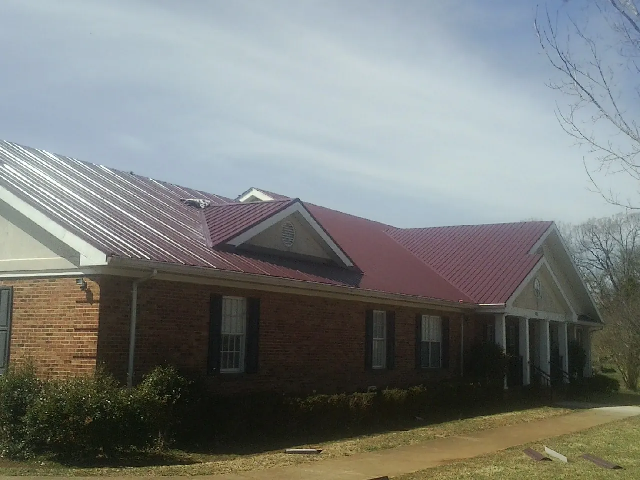 Red metal roof with gabled entries on a long brick building, from a Hail Damage Roof Repair job in Douglasville