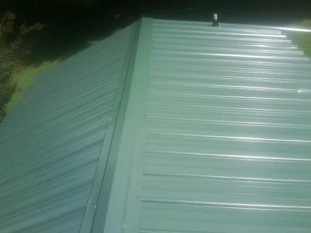 New green metal panels meeting at the ridge of a roof — Flat Roof Repair work by our crew in Douglasville
