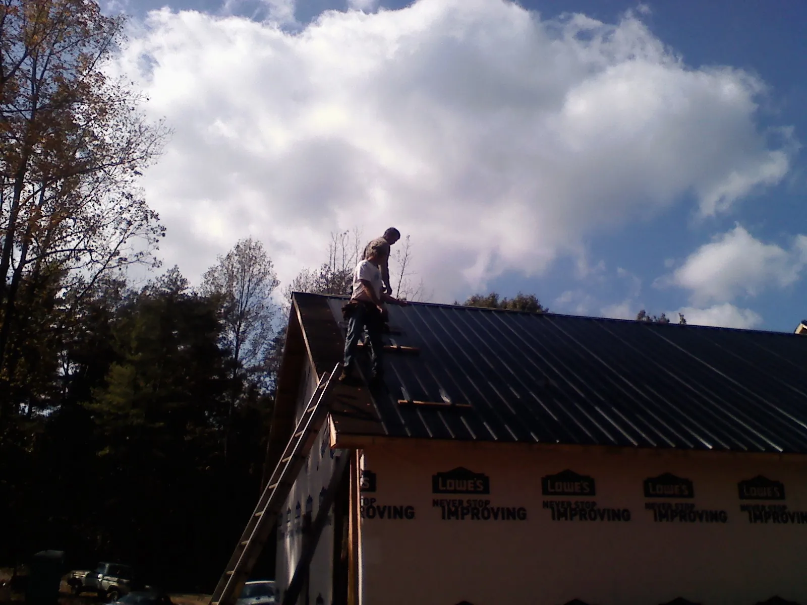 Roofer fastening dark metal panels high against a cloudy sky, from a Roof Inspection job in Douglasville