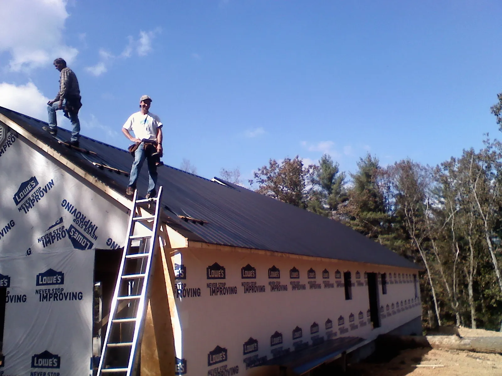 Two roofers standing on a long dark metal roof over a wrapped building in Douglasville