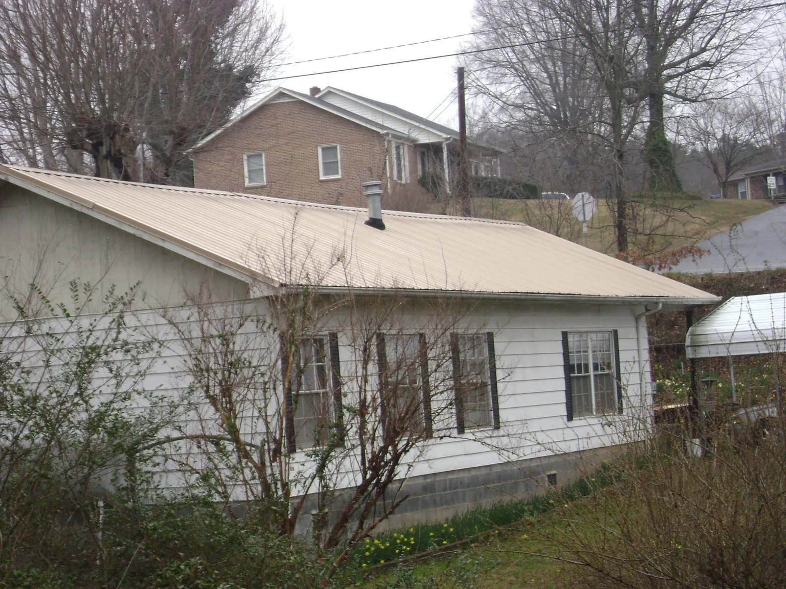 Tan metal roof on a white sided house set into a hillside — Commercial Roofing by Roofing Brothers in Douglasville